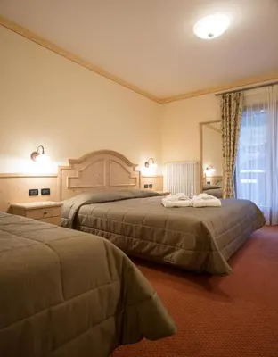 a hotel room with two beds and a mirror at Hotel Crepei in Pozza di Fassa