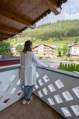 a woman standing on a balcony looking at a street at Hotel Crepei in Pozza di Fassa