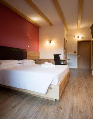 a bedroom with a large white bed and a table at Hotel Crepei in Pozza di Fassa