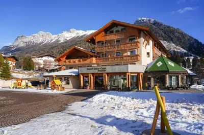 a large building in the snow in front of a mountain at Resort Dolce Casa - Family & Spa Hotel in Moena