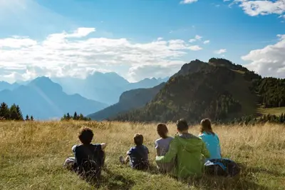 a group of people sitting on a hill looking at mountains at Sporthotel Europa Sul Lago in Alleghe