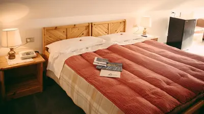 a bedroom with a bed with two lamps and two books at Sporthotel Europa Sul Lago in Alleghe