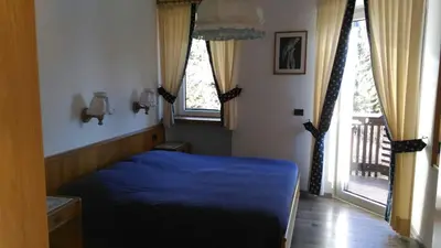 a bedroom with a blue bed and two windows at Park Hotel Miramonti in San Martino di Castrozza