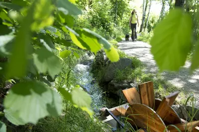 a woman walking a dog on a path next to a stream at Ferienwohnung im Haus Texel V in Parcines