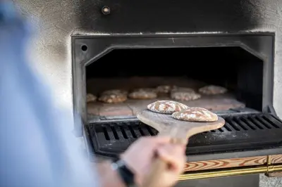 a person holding a cutting board in an oven with donuts at Taser Alm in Schenna