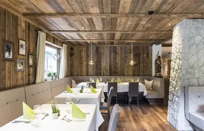 a restaurant with white tables and chairs and wooden walls at Hotel Florian in Selva di Val Gardena