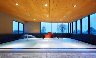 a swimming pool with a red chair in a room with windows at Apartments Heidenberger Fienili in Colle Isarco
