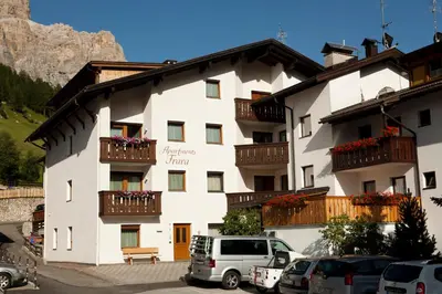 a white building with balconies and cars parked in a parking lot at Frara Residence Apartments in San Cassiano