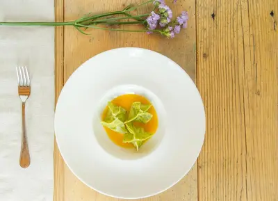 a white plate with a bowl of food on a table at Berghotel Miramonti in Tesero