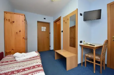 a bedroom with a bed and a desk and a television at Hotel Villa Agomer in Canazei
