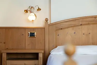 a bedroom with a wooden bed and a light on the wall at Family Hotel La Perla in Fiera di Primiero