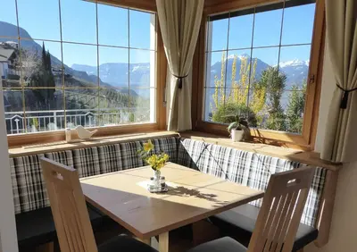 a table and chairs in a room with large windows at Garni Nunnemairhof in Schenna