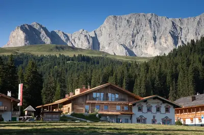 a building in a village with mountains in the background at Dolomites Living Hotel Tirler in Alpe di Siusi