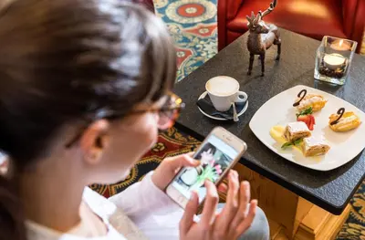 a woman sitting at a table using a cell phone at Hotel La Perla Wellness & Beauty in Canazei