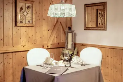 a dining table with two chairs and a chandelier at Hotel La Perla Wellness & Beauty in Canazei