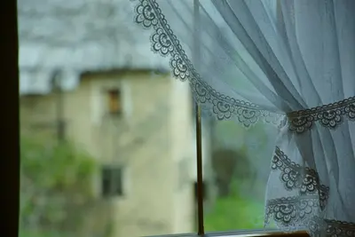 a window with a curtain with a house in the background at Agriturismo Grones in San Martino in Badia