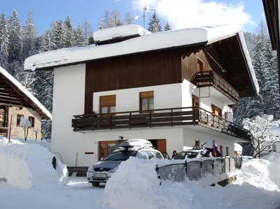 a house covered in snow with cars parked in front at Casa De Biasio PM in Falcade