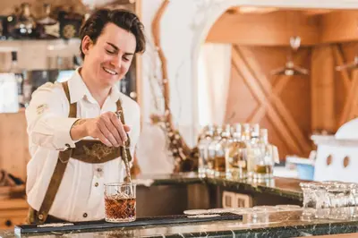 a man in a kitchen preparing a drink at Hotel Arnika in Pozza di Fassa