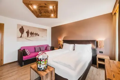 a bedroom with a large bed and a pink couch at Hotel Arnika in Pozza di Fassa