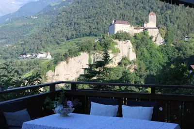 a balcony with a table and a castle on a mountain at Villa Falkner in Tirolo