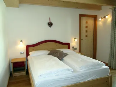 a bedroom with a bed with white sheets and a clock on the wall at Affittacamere Famiglia Ceschini in Tesero
