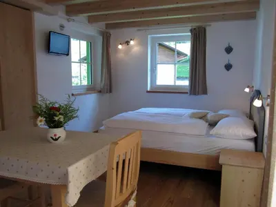 a bedroom with a bed and a table and two windows at Affittacamere Famiglia Ceschini in Tesero