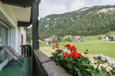 a balcony with red flowers and a chair and mountains at Chalet Pineta relax location in Canazei