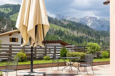a patio with a table and chairs and an umbrella at Ciasa La Rô in San Cassiano
