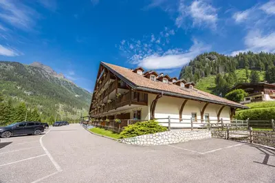a building in a parking lot with mountains in the background at Aparthotel Princess in Canazei