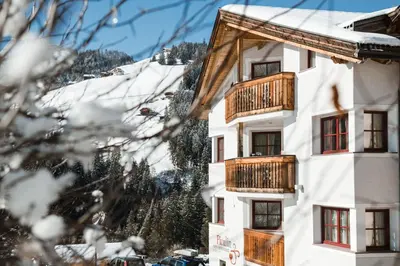 a white building with wooden balconies and a snow covered mountain at Piculin Alpin Apartments in San Martino in Badia