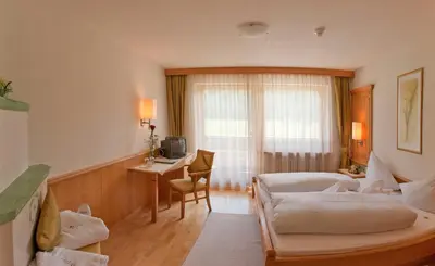 a hotel room with a bed and a desk at Hotel Brunnerhof in Rasùn di Sotto