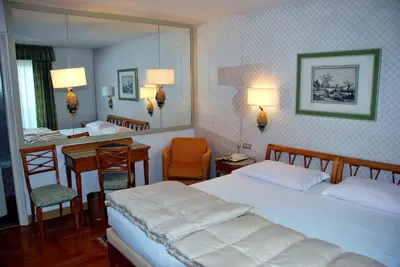 a bedroom with two beds and a desk and a mirror at Hotel De La Poste in Cortina dʼAmpezzo