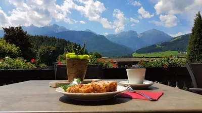 a table with a plate of food on a table with mountains at Hotel Scherer in Valdaora