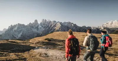 three people walking on a mountain with mountains in the background at Dolomites Smart Holidays in Valdaora