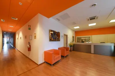 an office lobby with orange chairs and a counter at Hotel Fiera in Bolzano
