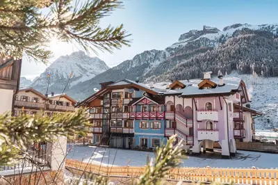 a large building with mountains in the background at B&B Family Accommodation Canazei SKI-IN SKI-OUT in Canazei
