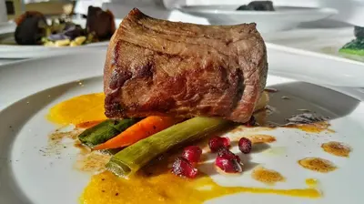 a plate of food with a piece of meat and vegetables at Hotel Arnika Wellness in Passo San Pellegrino