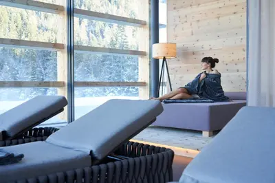 a woman sitting on a bed in a room with a window at Hotel Cristallo - Wellness Mountain Living in La Villa