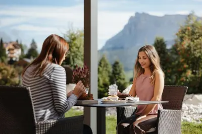 two women sitting at a table with a cake at Hotel Cristallo - Wellness Mountain Living in La Villa