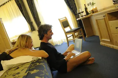 a man and woman sitting on a bed with a laptop at Family Hotel Andes - Only for Family in Vigo di Fassa