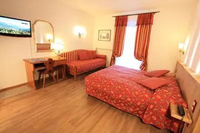 a bedroom with a bed and a desk and a couch at Hotel Trieste in Cortina dʼAmpezzo