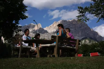 a group of people sitting at a picnic table in front of a mountain at Hotel Trieste in Cortina dʼAmpezzo