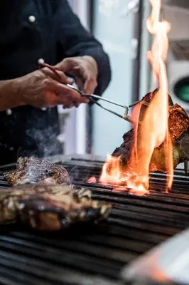 a person grilling meat on a grill with flames at Eggentaler in Bolzano