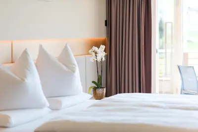 a hotel room with a bed with white pillows and a window at Weinegg Wellviva Resort in Appiano sulla Strada del Vino