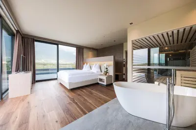 a bedroom with a tub and a bed with windows at Weinegg Wellviva Resort in Appiano sulla Strada del Vino