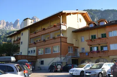 a large building with cars parked in a parking lot at Hotel Ladina in Campitello di Fassa