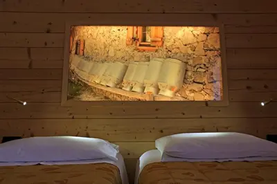 two beds in a room with a mirror on the wall at Hotel Ladina in Campitello di Fassa