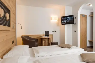 a bedroom with a bed and a desk with a computer at Hotel Garni Lastei in Pozza di Fassa