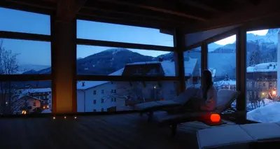 a woman sitting on a chair in a room with windows at Hotel Paladin in San Martino di Castrozza