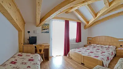 a bedroom with two beds and a desk and a window at Hotel Miramonti in Vigo di Fassa